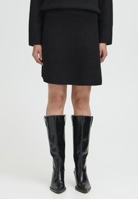 Zwarte gebreide mini-jurk met een geribde tailleband, gecombineerd met kniehoge zwarte leren laarzen met spitse neuzen en zijaccenten.