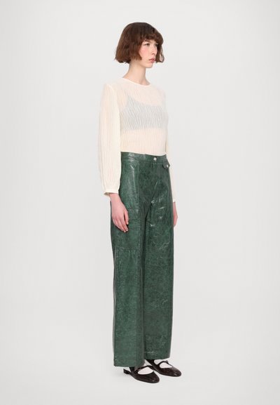 Witte top met lange mouwen van textuurstof, gecombineerd met hooghals groene leren broek met voorzakken en een recht gesneden ontwerp.