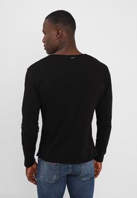 Zwarte langslijfshirt met een ronde hals, gemaakt van lichtgewicht stof en subtiele stiksels bij de halslijn en mouwen.