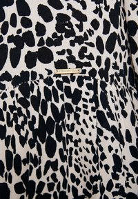Tessuto a stampa leopardata bianco e nero con un design plissettato e un piccolo cartellino metallico etichettato "SUPERDRY {Edit}" attaccato al bordo.
