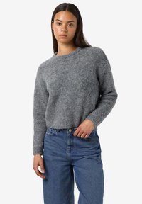 Grauer Strickpullover mit Rundhalsausschnitt und langen Ärmeln, kombiniert mit blauen, locker sitzenden Jeans. Weicher Stoff, bequeme Passform.