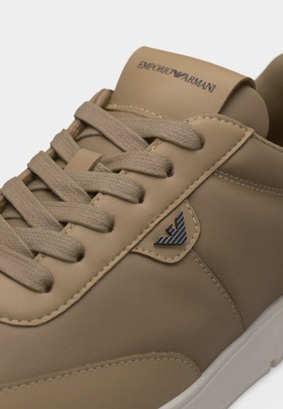 Μπεζ αθλητικό παπούτσι με κορδόνια, με το λογότυπο Emporio Armani στη γλώσσα και μεταλλικό έμβλημα στο πλάι, λευκή σόλα, ματ φινίρισμα.