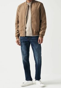 Veste bomber en daim marron, pull en laine léger gris clair, jean bleu foncé et baskets blanches. Design simple avec des poignets côtelés et une taille côtelée.