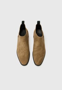 Botas de tobillo de ante marrón con puntera afilada, paneles laterales elásticos y una lengüeta verde en el talón. Suela negra con un mínimo de marcas en el interior.