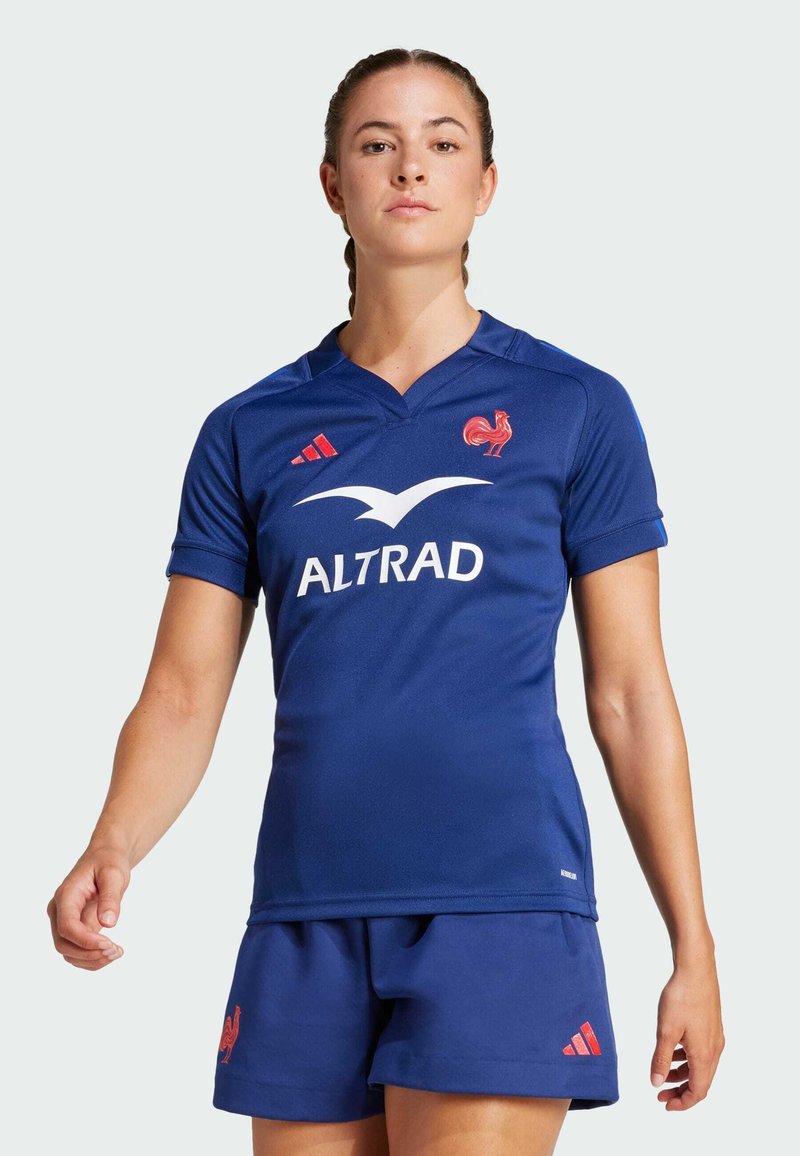 Jersey de rugby azul hecho de una tela suave, presenta un emblema de gallo rojo, un logo blanco y acentos rojos en el cuello. Combinado con pantalones cortos a juego.