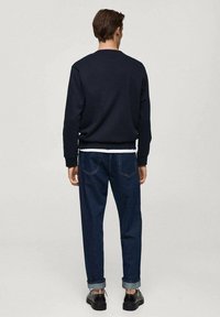 Felpa blu navy con colletto rotondo, polsini a costine, abbinata a jeans dritti scuri e scarpe nere. Design semplice e funzionale.