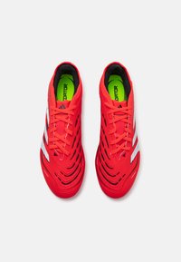 Rote Sportschuhe mit strukturierter Oberfläche, schwarzen Akzenten, silbernen Streifen und belüftetem Design. Die Schnürsenkel sind rot, mit einer leuchtend grünen Innensohle, die "PREDATOR" zeigt.