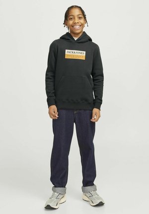 Felpa nera con un'applicazione rettangolare del logo in arancione e bianco, abbinata a jeans in denim blu scuro e sneakers grigie.