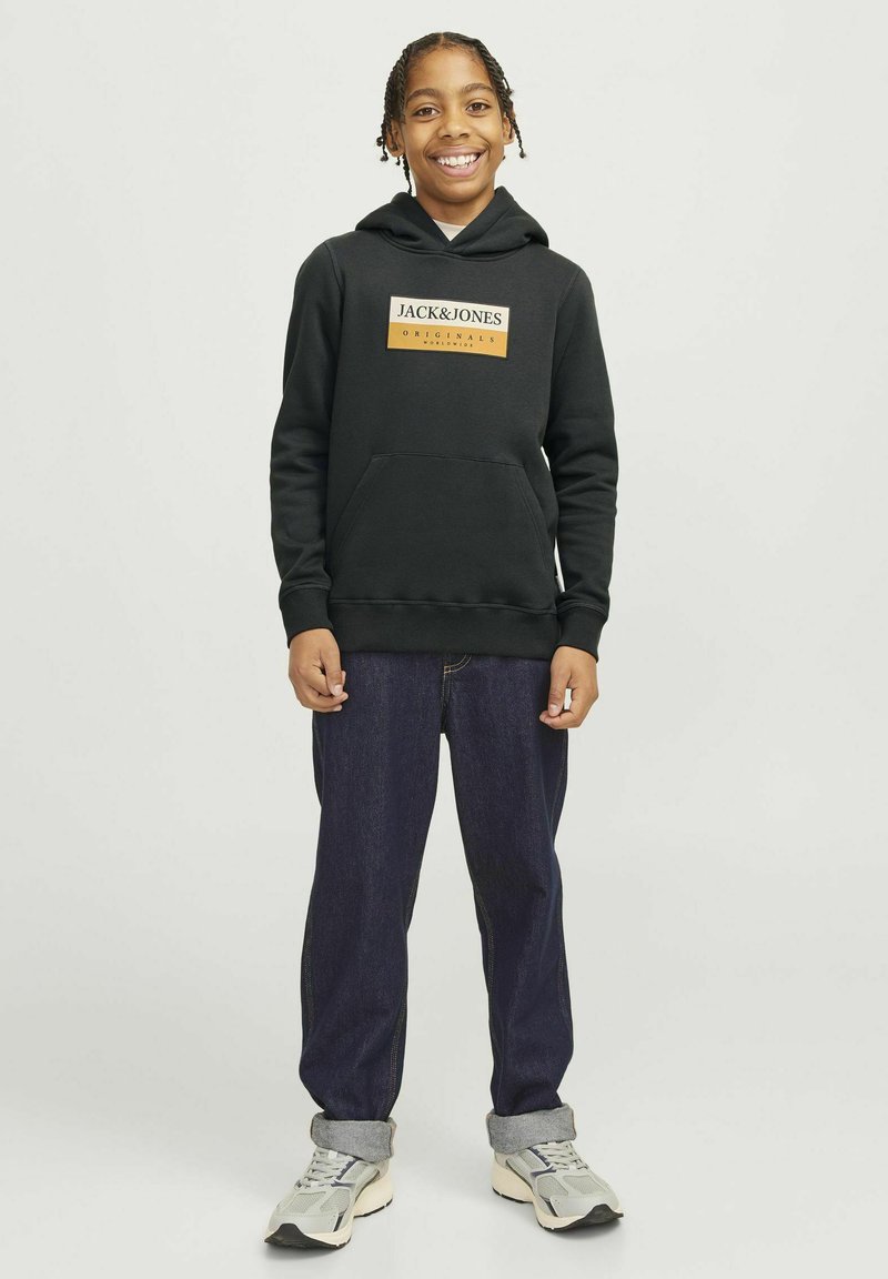 Sudadera negra con un parche de logo rectangular en naranja y blanco, combinada con jeans de mezclilla azul oscuro y zapatillas grises.