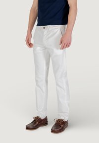 Pantaloni bianchi in cotone con vestibilità dritta, dotati di chiusura con bottone e tasche laterali, abbinati a scarpe da barca in pelle marrone.