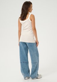 Débardeur rayé beige et blanc, associé à un jean en denim bleu à jambes larges. Le haut présente un col arrondi, et le jean a une coupe relax.