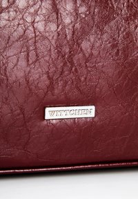 Sac en cuir bordeaux présentant une surface texturée et une plaque logo argentée "WITTCHEN", avec une forme rectangulaire et un design épuré.