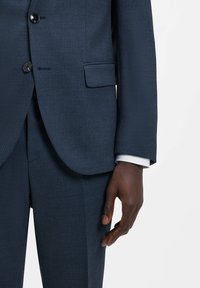 Completo blu scuro con tessuto strutturato. Caratteristiche notevoli includono un design monopetto, due bottoni e pantaloni a taglio dritto.