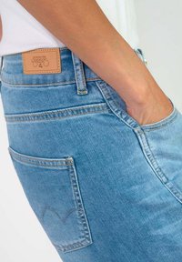 Jean en denim bleu clair au design ajusté, avec une étiquette en cuir à la taille et un détail de couture de poche unique.