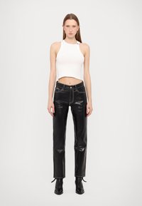 Top cropped branco com decote halter combinado com calças de pele pretas de cintura alta com costuras brancas em contraste e aberturas.