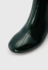 Botte cheville verte en cuir avec un bout arrondi, un design élégant, des détails de couture verticale et une texture brillante. Silhouette lisse et sculptée.