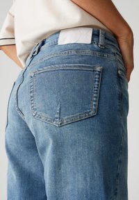 Blauwe denim jeans met een klassieke vijf-pocket ontwerp, middelhoge taille en een wit label op de achterste tailleband. Licht vervaagde textuur.