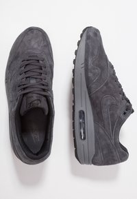 Šedé semišové sportovní boty s šněrováním, polstrovanou podrážkou a viditelnou vzduchovou jednotkou. Texturované detaily na svršku zvyšují přilnavost.