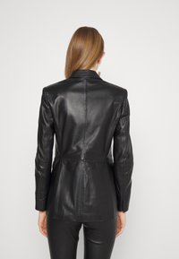 Černý kožený blazer s přiléhavým střihem, upravenou siluetou, vykrojeným klopovým límcem, švovými detaily a zapínáním na jeden knoflík.