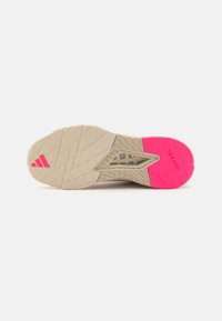 Talpă de pantof sport bej, cu un grip texturat, având un accent roz proeminent și un design cu modele pentru tracțiune. Logo-ul este situat pe lateral.