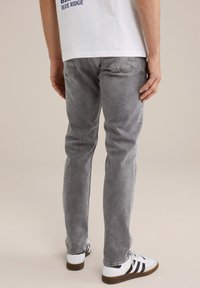 Jeans de mezclilla gris con un corte ajustado, cinco bolsillos y un ligero desgastado. Combinados con zapatillas blancas con rayas negras.