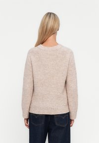 Ανοιχτό μπεζ πλεκτό πουλόβερ με στρογγυλή λαιμόκοψη, μακριά μανίκια και ελαφρώς κοντή σιλουέτα. Μαλακή υφή και ριμπ λεπτομέρεια στο τελείωμα.