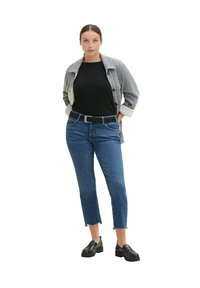 Szara i biała marynarka z kołnierzykiem na czarną bluzkę, niebieskie dżinsy do kostek i czarne półbuty. Cechy to ściśnięta talia i postrzępione brzegi.