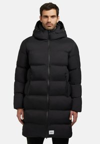 Sort pufferjakke med lynlås, hætte og sidelommer. Har et kviltet design med en puffy, isoleret struktur for varme.