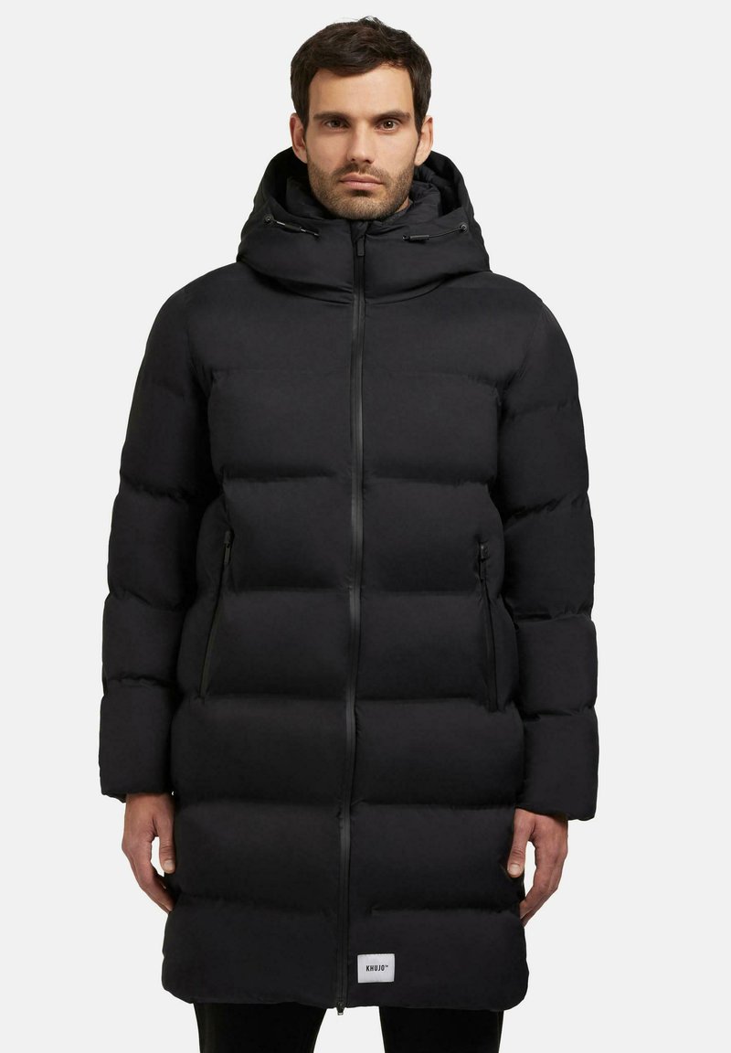 Sort pufferjakke med lynlås, hætte og sidelommer. Har et kviltet design med en puffy, isoleret struktur for varme.