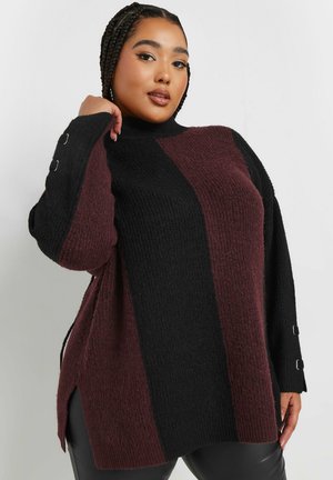 Jersey de punto grueso en burdeos y negro con cuello alto, mangas largas y aberturas laterales. Presenta herrajes plateados en los puños. Acabado texturizado.