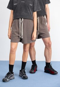 Grå shorts med elastisk midjebånd og hvite snorer, sammen med svarte T-skjorter og svarte sportssko med røde detaljer.
