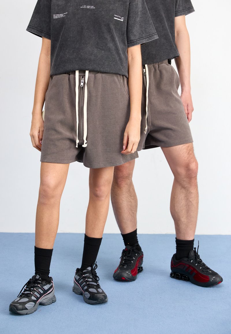 Grå shorts med elastisk midjebånd og hvite snorer, sammen med svarte T-skjorter og svarte sportssko med røde detaljer.