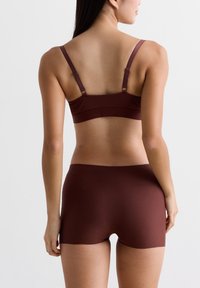 Vrouw van achteren afgebeeld in een bijpassende bruine naadloze bh met verstelbare bandjes en hoge boyshort onderbroek.