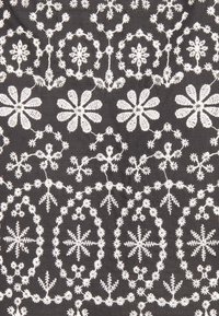 Schwarzer Stoff mit aufwendigen weißen gestickten Mustern, die Blütenformen, geometrische Designs und verbindende, rankartige Details aufweisen.