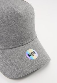 Casquette grise en tissu doux, avec une couronne arrondie, un bord incurvé et un logo circulaire brillant avec "DJINNS" imprimé de manière proéminente.