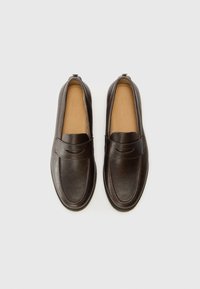 Mocasines de cuero marrón con un acabado suave, presentan una puntera redondeada y una correa decorativa a lo largo de la parte superior. Diseño de suela plana.