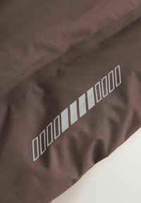 Tissu marron présentant une surface texturée avec une série de motifs rectangulaires et rayés blancs le long d'un bord.