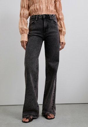 Vaqueros negros acampanados con una cintura alta y un ligero desvanecimiento, combinados con una blusa de manga larga color durazno claro con detalles fruncidos.