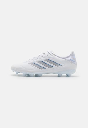 Chaussure de football blanche avec un dessus en synthétique lisse, des accents bleu clair, trois rayures grises et une semelle moulée avec des crampons courts.