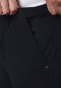 Czarne spodenki z teksturowanej tkaniny, z dopasowaną talią, bocznymi kieszeniami oraz subtelnym logo na biodrze. Zbliżenie na materiał i krój.