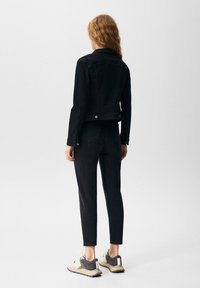 Chaqueta de denim negro y pantalones a juego, ambos ajustados, con una textura suave. Los zapatos son grises con acentos en negro y blanco, y cuentan con una suela robusta.