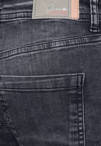 Jeans de mezclilla negra con una vista en primer plano de las costuras cosidas, un bolsillo trasero y una etiqueta. La tela tiene una textura suave.