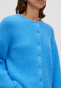 Lichtblauwe gebreide cardigan met een gestructureerd patroon, ronde halslijn en vijf bijpassende knopen aan de voorkant. Zacht, comfortabel materiaal.