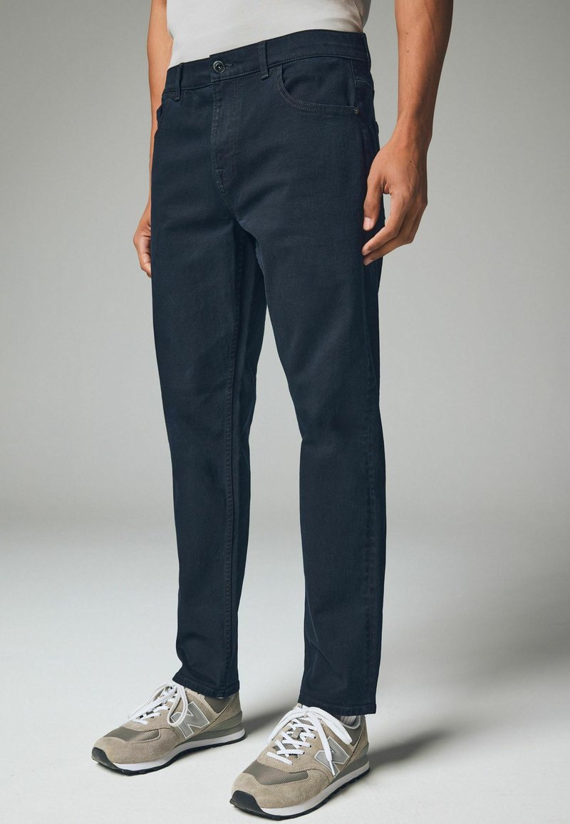 Marineblauwe denim jeans met een rechte pasvorm, uitgerust met een knoopsluiting, riemlussen en vijf zakken. Draag met grijze sneakers.