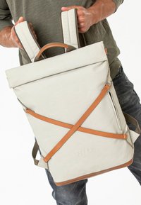 Zaino roll-top in tessuto grigio chiaro con spallacci in pelle marrone, che presenta un design elegante, spallacci regolabili e una tasca laterale con zip.