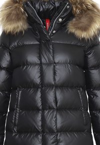 Giacca a vento nera con design trapuntato, dotata di cappuccio in pelliccia marrone removibile, chiusura con zip e due tasche laterali.