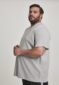 T-shirt en coton gris, col rond, manches courtes, coupe décontractée, texture douce, porté avec un short noir à bandes blanches sur les côtés.