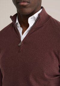 Pull bordeaux zippé avec col côtelé et fermeture éclair argentée, porté sur une chemise blanche boutonnée. Texture douce, design décontracté.