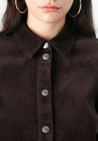 Brown corduroy shirt with a pointed collar, metal snap buttons, and ribbed texture. Displays a close-up of the upper portion.