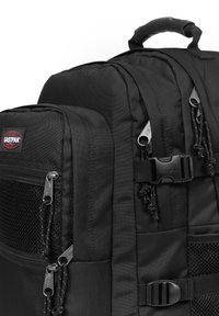 Zaino in tessuto nero con più scomparti con zip, tasca in rete testurizzata e spallacci regolabili. Presenta il logo Eastpak e una maniglia robusta.